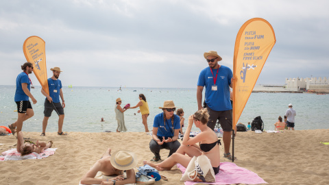 Dos informadores conversan de la nueva prohibición de fumar con bañistas, en la playa del Bogatell (Barcelona).
