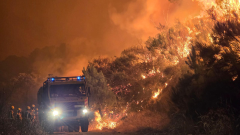 Un camión de bomberos circula entre las llamas, que observan un grupo de operarios, la noche del pasado miércoles en el Barranco de las Cinco Villas (Ávila).