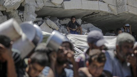 Niños piden comida en Gaza Gaza City (-), 04/08/2025.- A boy (rear) sitting among the rubble of a damaged building looks on as internally displaced Palestinians gather to receive food from a charity kitchen, in Gaza City, Gaza Strip, 04 August 2025. Humanitarian organizations have warned of an imminent food catastrophe for thousands of children, a crisis caused by severe food insecurity, a decline in health services, and ongoing restrictions on humanitarian aid and essential supplies. EFE/EPA/MOHAMMED SABER
