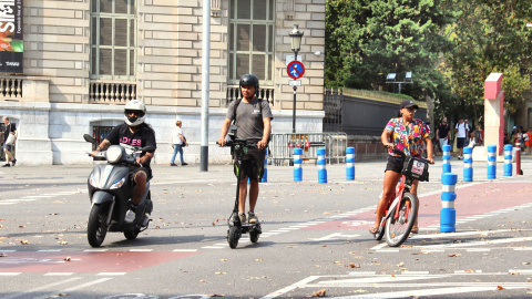 Una moto, un patinet i una bici circulen per un carrer de Barcelona Una moto, un patinet i una bici circulen per un carrer de Barcelona