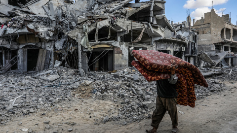 Un hombre camina con colchones entre edificios destruidos. 10/10/2025 ONLY FOR USE IN SPAIN