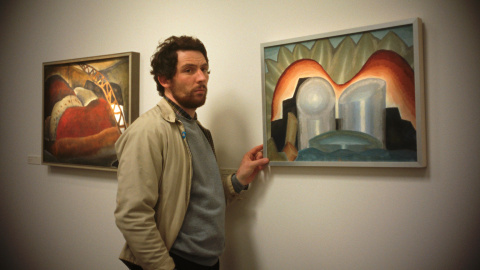 El personaje, al lado de los cuadros de Arthur Dove que quiere robar (Mubi) Fotograma de 'The Mastermind'.