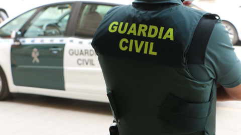 Imagen de archivo de un agente de la Guardia Civil, de espaldas, junto a un vehículo oficial.