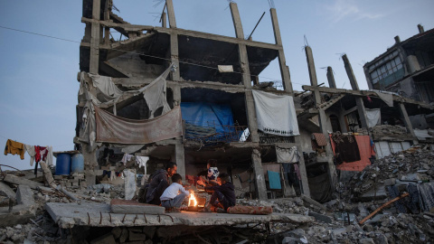 Palestinos desplazados se calientan junto a una fogata entre las ruinas de su hogar destruido en Khan Yunis, sur de la Franja de Gaza, el 30 de diciembre de 2025.