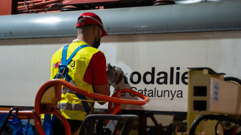 Un treballador neteja el logotip de Rodalies en un tren estacionat a una base de manteniment Un treballador neteja el logotip de Rodalies en un tren estacionat a una base de manteniment