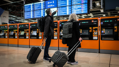 Dos usuaris miren les pantalles de l'estació de Sants amb els horaris dels trens. Dos usuaris miren les pantalles de l'estació de Sants amb els horaris dels trens.