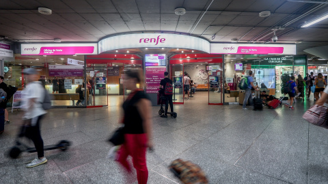 Viajeros pasan por delante de la oficina de Renfe, en la estación de Atocha.