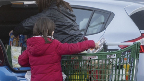 Una mujer y una niña meten la compra en el maletero de su vehículo, al salir de un supermercado.