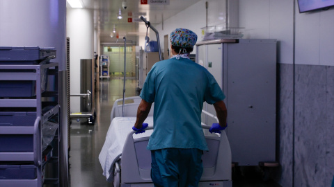 Un celador transporta una camilla vacía en el pasillo.