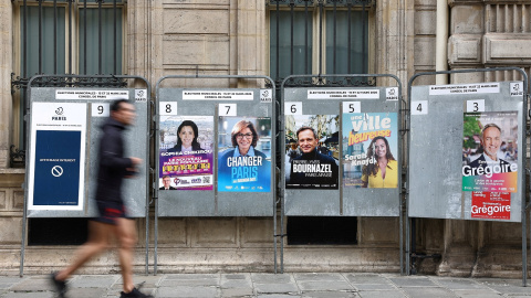 Un hombre corre junto a carteles de campaña electoral con los candidatos a la alcaldía de París.
