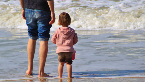 Un padre y su hija observan el mar desde la orilla.