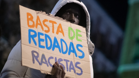 Una persona sujeta un cartel durante la XIII Marcha por la Dignidad, en Lavapiés, a 6 de febrero de 2026.