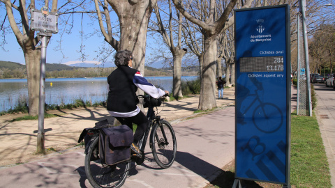 Una dona anant amb bici a l'estany de Banyoles i el comptador de bicicletes que s'hi ha instal·lat
