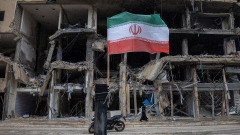 Una bandera iraní ondea mientras una mujer camina junto a un edificio destruido tras los ataques de Israel en los suburbios del sur de Beirut, Líbano.