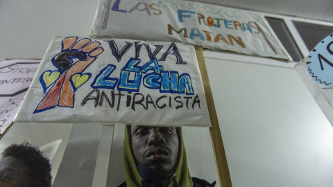 Una persona entre pancartas durante un acto de conmemoración por el aniversario de la tragedia de la playa de El Tarajal.