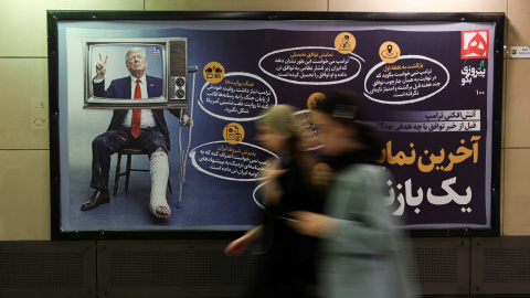 Dos mujeres pasan junto a un letrero con una imagen que representa al presidente de EEUU  Donald Trump herido, en Teherán, el 17 de junio de 2026.