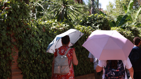 Varias personas se refugian del sol con paraguas en Sevilla.
