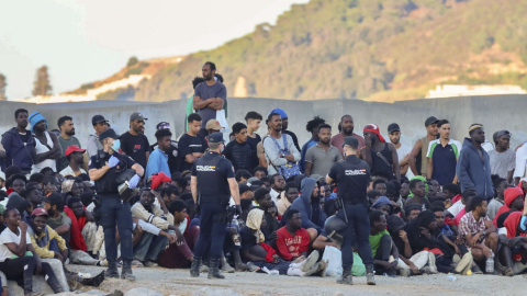 Personas migrantes y agentes de Policía en la playa ‘El Trampolín’ de Ceuta.