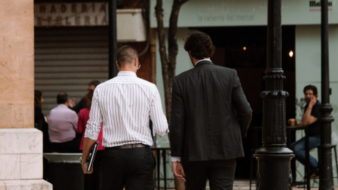 Dos hombres con traje de negocios caminando por una acera urbana Dos hombres con traje de negocios caminando por una acera urbana