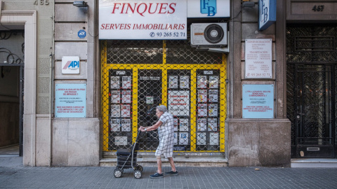 Una dona passeja davant d'una immobiliària a Barcelona. 30/03/2026 Una dona passeja davant d'una immobiliària a Barcelona.
