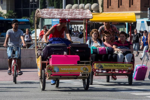 Varios turistas se desplazan en bici-taxi mientras los taxistas mantienen las concentraciones en el centro de la ciudad con motivo de la huelga iniciada el pasado 25 de julio por el conflicto de las licencias VTC (alquiler de vehículos con conductor) tra