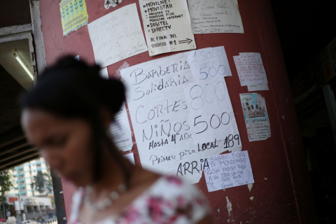 Una mujer pasa junto a una columna en Caracas en la que están colocados anuncios de bienes y servicios ofrecidos por particulares. REUTERS/Andres Martinez Casares