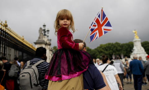  Una niña sujeta una bandera británica mientras numerosas personas se congregan frente al Palacio de Buckingham para rendir tributo a la reina Isabel II, este sábado en Londres.- EFE