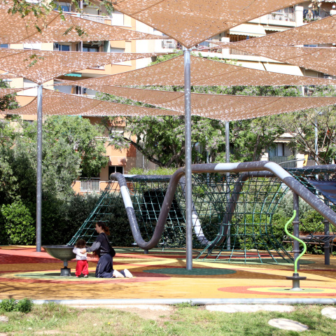 Una persona juga amb un infant en una zona amb ombra en un parc a Barcelona