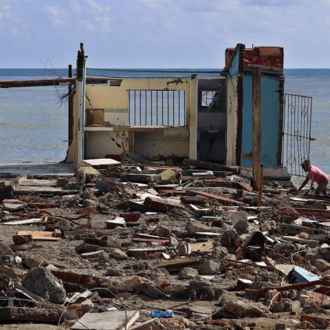 Personas caminan frente a una casa destruida, en Guamá, Santiago de Cuba.