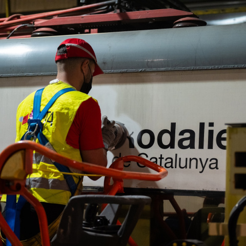 Un treballador neteja el logotip de Rodalies en un tren estacionat a una base de manteniment