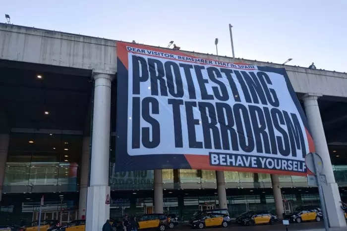 Òmnium desplega una pancarta gegant a l'aeroport del Prat: "A Espanya, protestar és terrorisme"