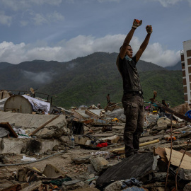 Un voluntario hace el gesto que reclama silencio sobre los escombros de un edificio en La Guaira.
