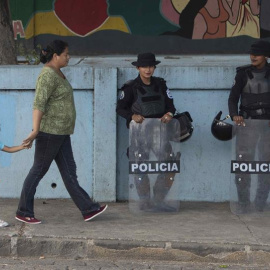 Una mujer con su hija de la mano caminan frente a dos agentes de la Policía en una avenida de Managua (Nicaragua). EFE/Jorge Torres