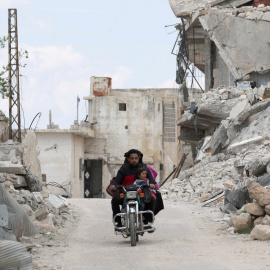 Una familia viaja en una moto cerca de los escombros de los edificios dañados en la región siria de Jabal al-Zawiya. REUTERS / Khalil Ashawi