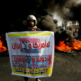 Un manifestante iraquí lleva un cartel que dice: "No Estados Unidos ni Irán, No dólar y No Toman, lealtad solo a Irak" junto a la quema de neumáticos para bloquear una carretera durante las protestas contra el gobierno en Najaf. REUTERS / Alaa al-Marj