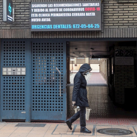 Una mujer camina ante una clínica dental que informa de su cierre debido al coronavirus, en Zaragoza. EFE/ Javier Cebollada