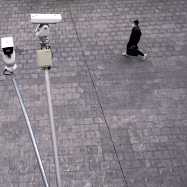 Un hombre con mascarilla camina por Shanghai, bajo unas cámaras de vigilancia en la calle. REUTERS/Aly Song