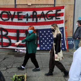 Varias personas pasan por delante de una bandera estadounidense vuelta del revés, en protesta contra el racismo, en el edificio del Recinto Este del Departamento de Policía de Seattle, en la autoproclamada Zona Autónoma de Capitol Hill. REUTERS / Goran