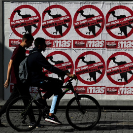 Dos jóvenes pasan junto a un muro empapelado con carteles contra el pago de la deuda, en Buenos Aires (Argentina). REUTERS/Agustin Marcarian