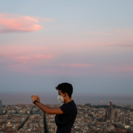 Un jóven, con mascarilla, toma una foto con su 'smartphone', con la ciudad de Barcelona al fondo. REUTERS/Nacho Doce