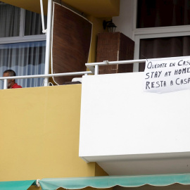 Un hombre se asoma al balcón de una vivienda junto a un cartel que invita a los paseantes a quedarse en casa en varios idiomas en la localidad turística de Los Cristianos (Tenerife).EFE/Ramón de la Rocha