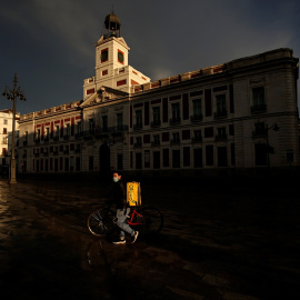 Un repartidor de Glovo con mascarilla pasa por una prácticamente desierta Puerta del Sol, de Madrid. REUTERS/Juan Medina