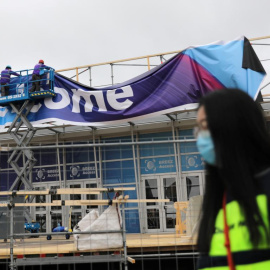 Una mujer con mascatilla pasa por delante de unos operarios que desmontan las lonas del Mobile World Congress, de Barcelona, tras su cancelacion. REUTERS/Nacho Doce