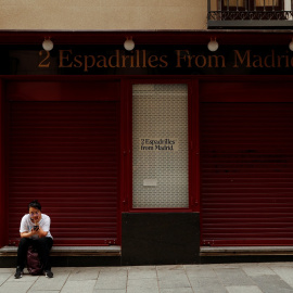 Una joven mira su móvil, sentada en la puerta de una tienda cerrada en el centro de Madrid. REUTERS/Susana Vera
