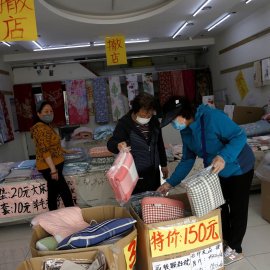 Unos clientes con mascarillas compran ropa de cama en una tienda de ropa para el hogar con avisos de liquidación, en Pekín.. REUTERS / Tingshu Wang