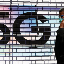Un hombre con mascarilla hablando por su móvil, pasa delante del logo de la tecnología 5G, en una calle de Londres. REUTERS/John Sibley