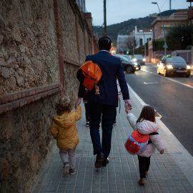 Dos niñas de la mano con un hombre camino del colegio, en Barcelona. EUROPA PRESS/David Zorrakino