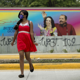 Una joven con mascarilla pasa frente a un cartel del presidente de Nicaragua Daniel Ortega y su esposa Rosario Murill, en Managua. EFE/Jorge Torres