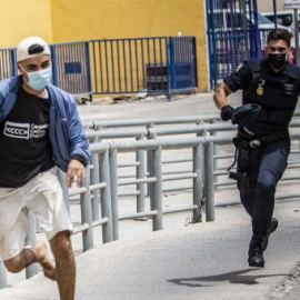  Un joven migrante intenta escapar de las naves del Tarajal en Ceuta mientras es perseguido por dos policías. -Jairo Vargas / ARCHIVO