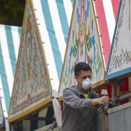 Un operario con mascarilla desmonta una caseta en las instalaciones de la Feria de Abril de Sevilla. EUROPA PRESS/María José López